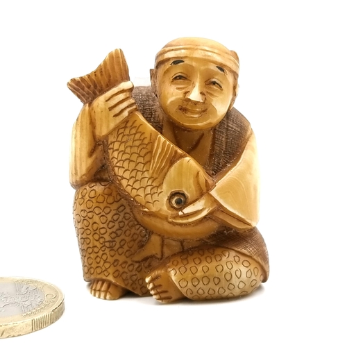 518 - A carved bone Netsuke figure of a seated Gentleman holding a carp with signed detailing to base. Dim... 