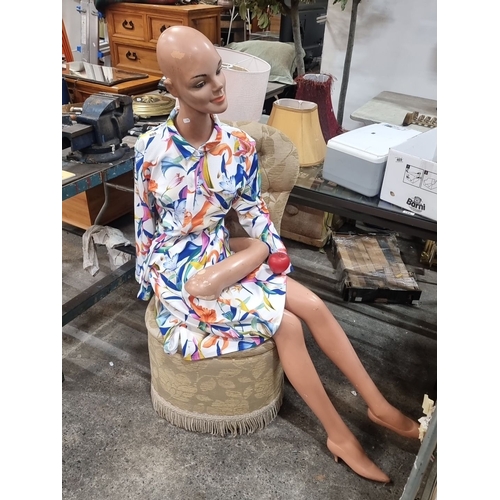 808 - Vintage mannequin dressed in a floral dress, seated on an upholstered round stool with fringe trim. ... 