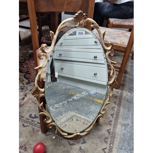 838 - A vintage Ornate oval wall mirror with a decorative gilt frame featuring intricate scrollwork. Likel... 