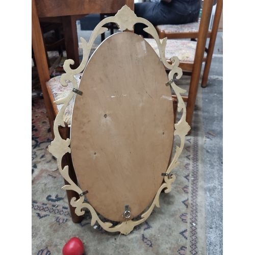 838 - A vintage Ornate oval wall mirror with a decorative gilt frame featuring intricate scrollwork. Likel... 