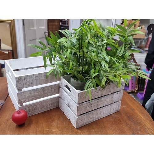 899 - A set of two rustic white wooden crates with artificial green foliage in a metal cylindrical vase.