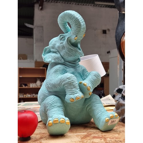 391 - A characterful figure of a cheerful baby elephant in a turquoise shade with gold toned nails and tus... 