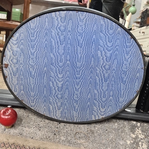 715 - Antique oval-shaped mirror with ornate black frame and blue patterned backing.