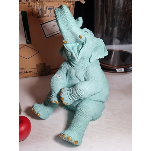 391 - A characterful figure of a cheerful baby elephant in a turquoise shade with gold toned nails and tus... 