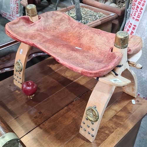 744 - Carved wooden bcamel stool with brass accents and embossed leather seat, featuring a red decorative ... 