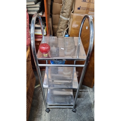 766 - A Chrome-plated metal utility cart with three perforated shelves and four caster wheels for easy mob... 