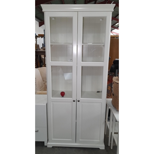 955 - A glass fronted double door display unit. Features three shelves plus two additional hidden shelves.... 