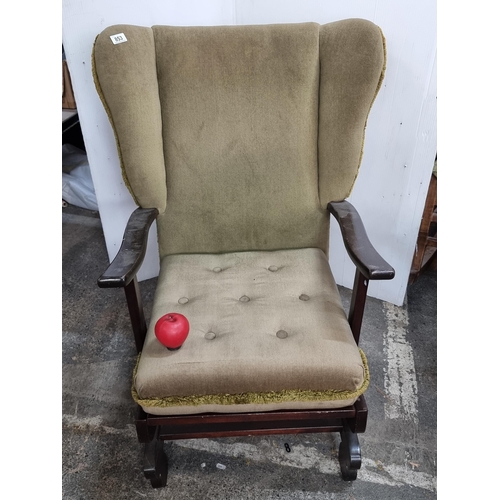 853 - A vintage wingback wooden framed rocking chair upholstered in a mint green velvet like fabric