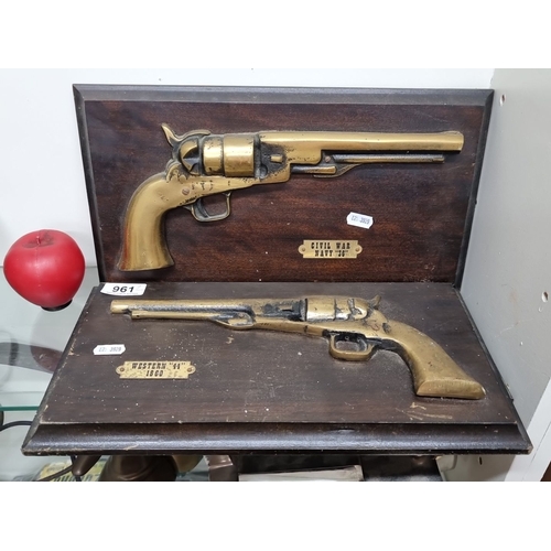 961 - Two brass replica pistols mounted on a wooden display, marked 