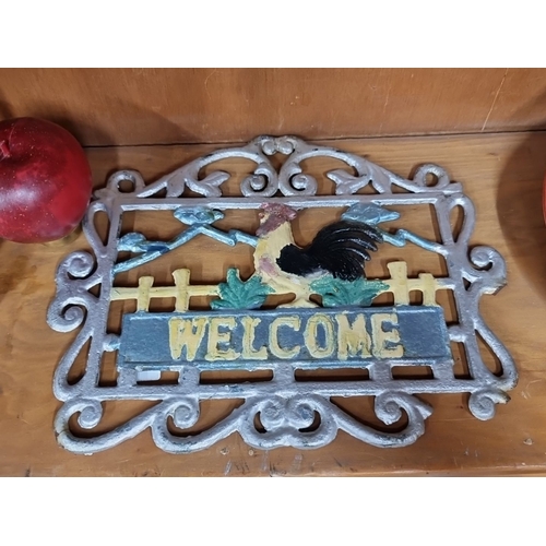 1008 - A cast iron sign with a colorful rooster and foliage design. Decorative scrollwork accents. Measures... 