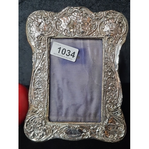 1034 - An elaborately engraved antique sterling silver photo frame with floral and scroll motifs, velvet ba... 