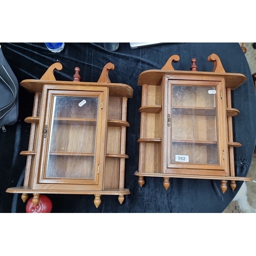 992 - A pair of vintage wooden wall-mounted display cabinets with glass doors and shelves. Each features e... 