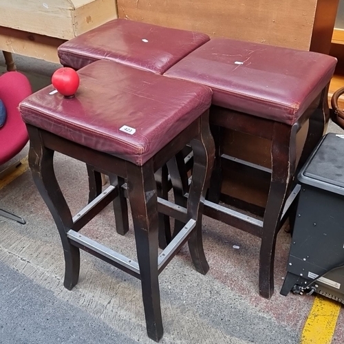 423 - A set of three vintage Irish made bar stools. with dark wood frames and red cushioned seats. They we... 