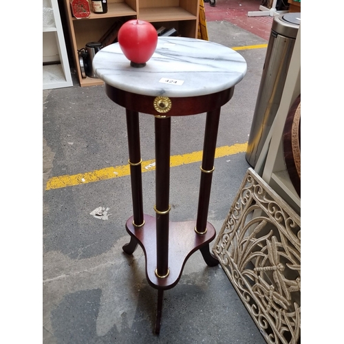 424 - Mahogany plant stand with white marble top. Displays four slender legs accented with brass rings.