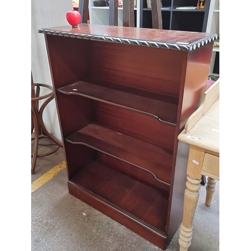 443 - A mahogany bookshelf featuring two shaped shelves and braided edging.