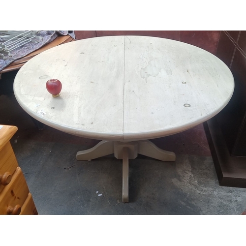 1029 - Round wooden dining table with a central pedestal base, finished in a distressed vintage white paint... 