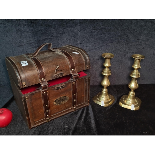 920 - A vintage wooden chest featuring leather straps along with a pair of tall brass candle sticks.