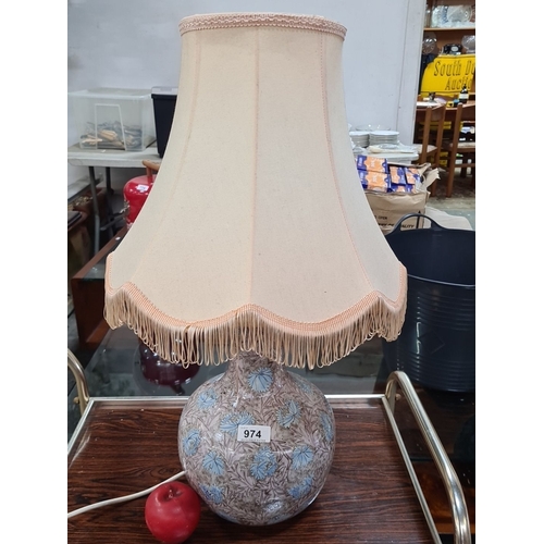 974 - Ceramic table lamp features floral patterns and a fringed fabric shade, marked at the base.