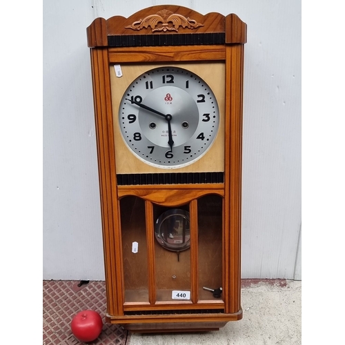 440 - Vintage wooden wall clock with decorative carvings, circular dial, and visible pendulum.