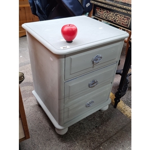 487 - A handsome  wooden nightstand with three drawers, featuring glass knobs and a unique red knob accent... 