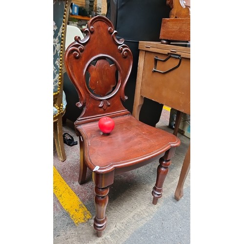 479 - An antique shield back hall chair with intricately carved backrest and turned legs, finished in a ri... 