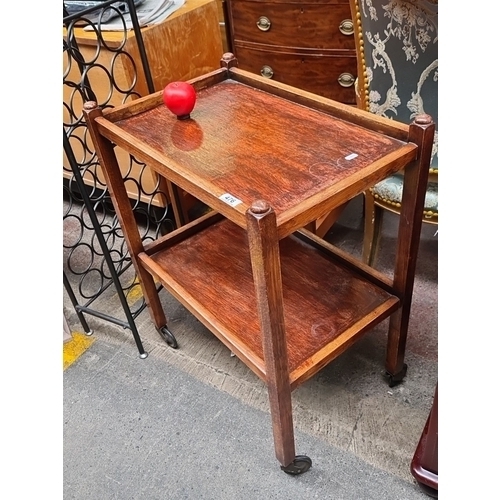 476 - Vintage wooden two-tier side table. Solid frame with rounded corners and castor wheels for mobility.