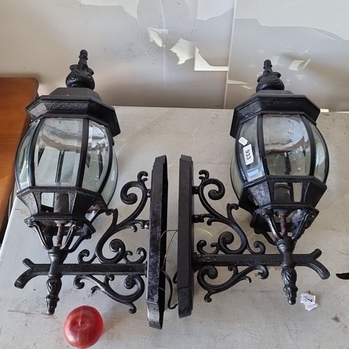 933 - Pair of Victorian-style wrought iron outdoor wall lanterns with ornate scrollwork and clear glass pa... 