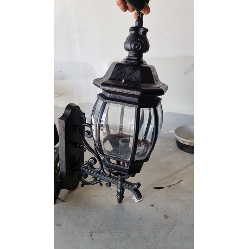 933 - Pair of Victorian-style wrought iron outdoor wall lanterns with ornate scrollwork and clear glass pa... 