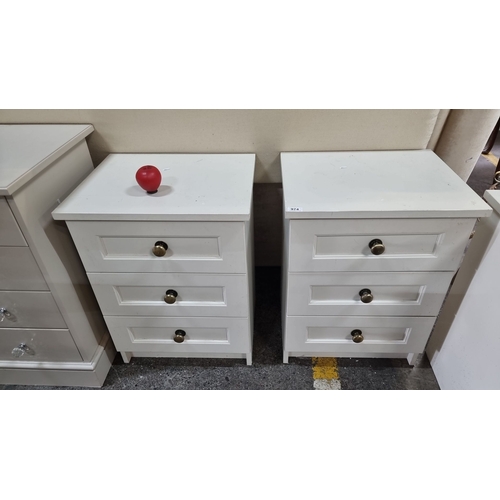 974 - Pair of white wooden three-drawer bedside tables with brass knobs, featuring light oak interiors. Th... 