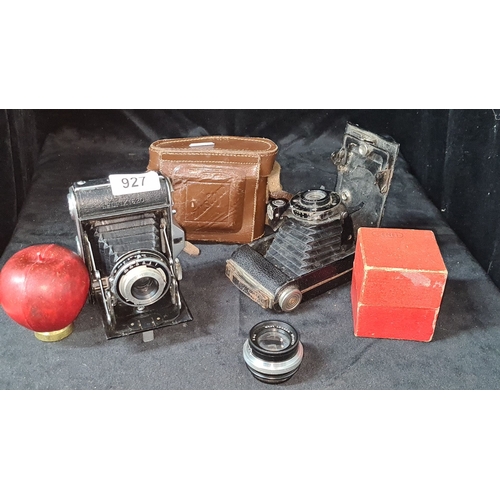 1100 - Includes two vintage cameras with bellows, one in a leather case, an additional lens, and a red box.... 