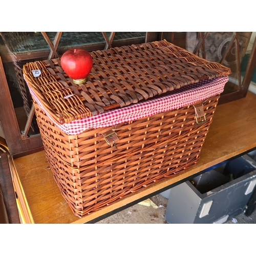 942 - A large Woven wicker picnic basket with hinged lid, dual brass clasps, and red gingham fabric lining... 