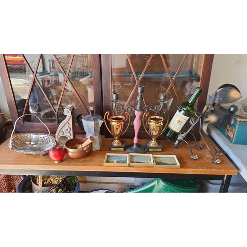 Collection of eclectic items including two brass trophies, a metal wine holder, a pair of candelabras, a decorative pestle and mortar set, a moka pot, a carved wall bracket, and a wire serving basket, accompanied by three small framed landscape paintings.