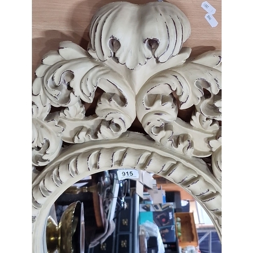 915 - Baroque-style carved mirror with ornate floral detailing, creamy white finish. Approximately 80 cm i... 