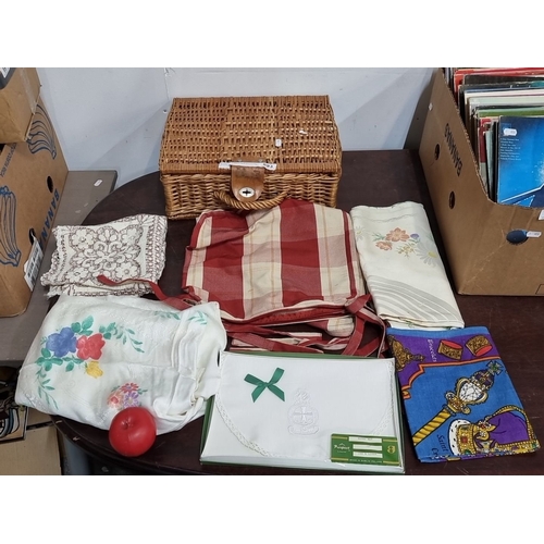 893 - Wicker picnic basket with assorted vintage linens, including embroidered and printed tablecloths. Ap... 