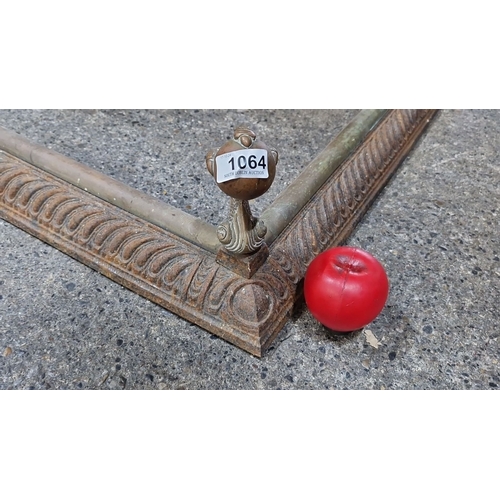 1064 - Ornate cast iron fireplace fender with brass finials, featuring a decorative scroll motif and ball a... 