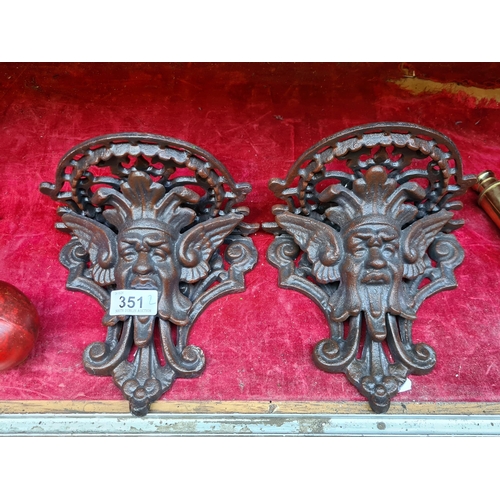 351 - A pair of heavy cast metal wall shelves, with decorative faces and mount for screwing to the wall.