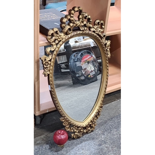 734 - Gilt-framed oval mirror, featuring intricate floral motifs, from the Victorian era.