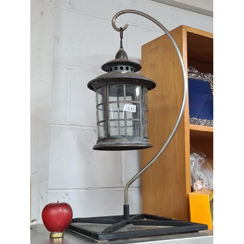 1142 - A vintage metal and glass fronted lantern held on a curved stand cast iron stand.