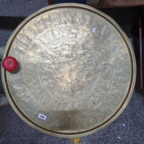 498 - Ornate brass tray table with intricate engravings, supported by an elaborately carved wooden base.