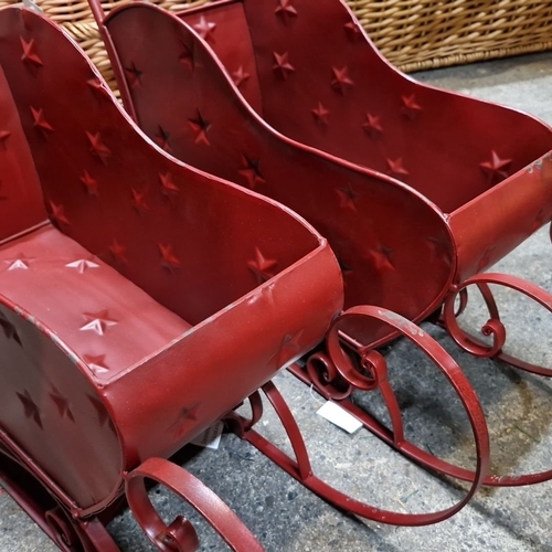 678 - Pair of new decorative red metal sleighs, featuring embossed star details and elegant scrollwork run... 