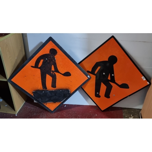 972 - Set of two vintage roadwork signs feature bold black figures on reflective orange backgrounds.