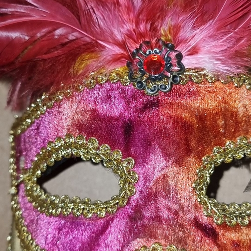 981 - Two decorative masquerade masks. One with vibrant pink feathers and a gemstone accent; the other is ... 