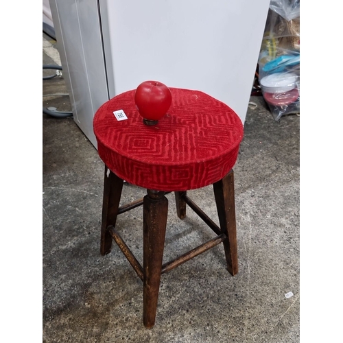 Vintage wooden stool with red upholstered seat. Sturdy construction and rustic charm, showcasing simple and functional design elements.