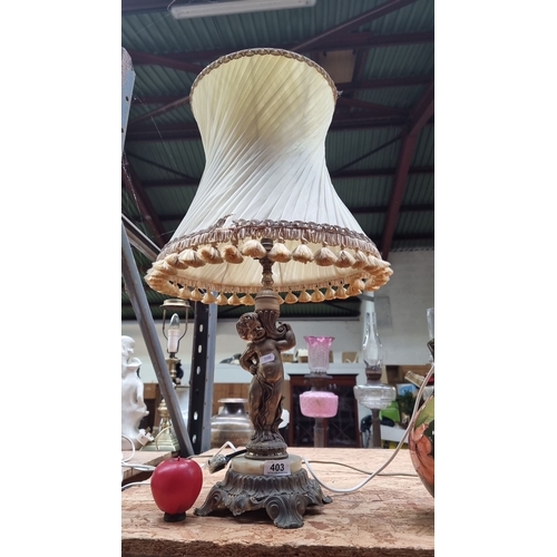 403 - Antique brass table lamp features a cherub figure base with a pleated fabric shade and tassel fringe... 