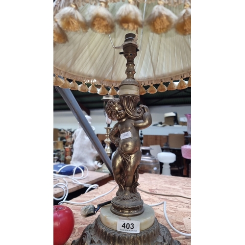 403 - Antique brass table lamp features a cherub figure base with a pleated fabric shade and tassel fringe... 