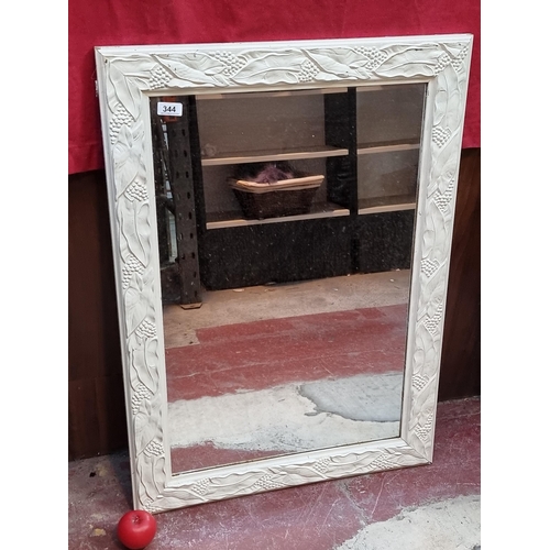 344 - A large mirror housed in a white fainted frame featuring foliate design in relief. MM: 65cm x 90cm