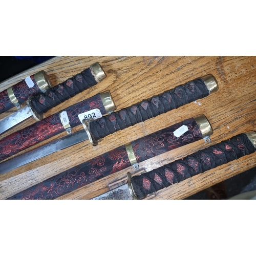 802 - Set of three decorative katana swords with intricately patterned black and red woven handles and sca... 