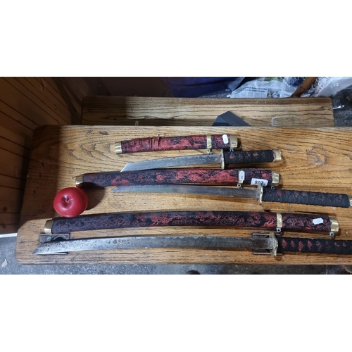 802 - Set of three decorative katana swords with intricately patterned black and red woven handles and sca... 