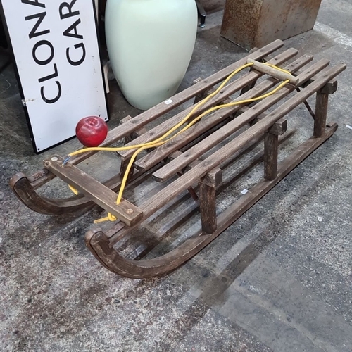 1106 - A Vintage wooden sled with sturdy slatted design and yellow pull rope. Offers a classic winter aesth... 