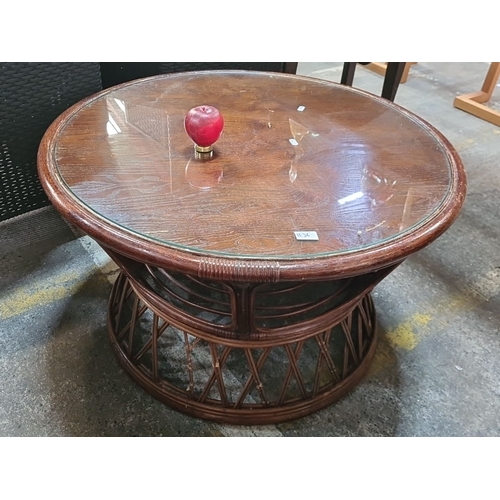 1136 - A Round glass-topped rattan coffee table with wood veneer surface.